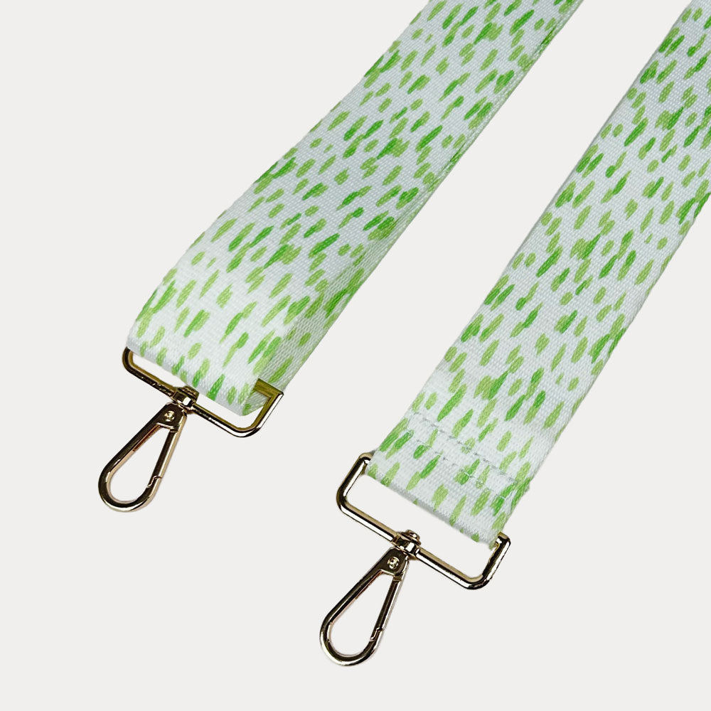 Green and white dot patterned bag strap with gold hardware on a light gray background
