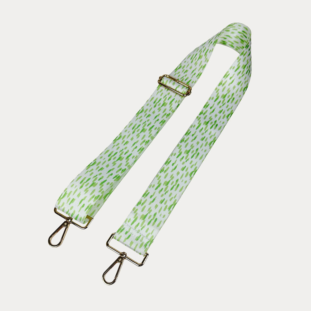 Green and white dot patterned bag strap with gold hardware on a light gray background