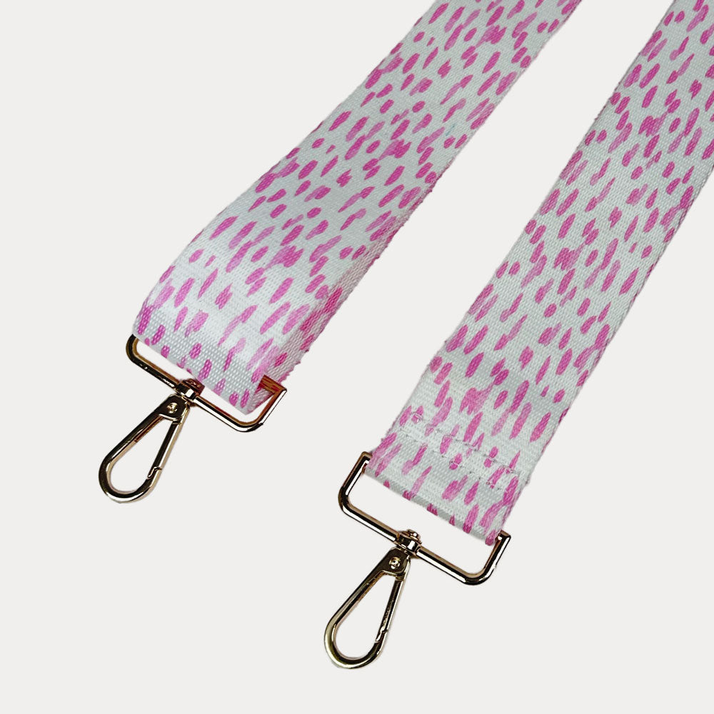Pink and white dot patterned bag strap with gold hardware on a light gray background