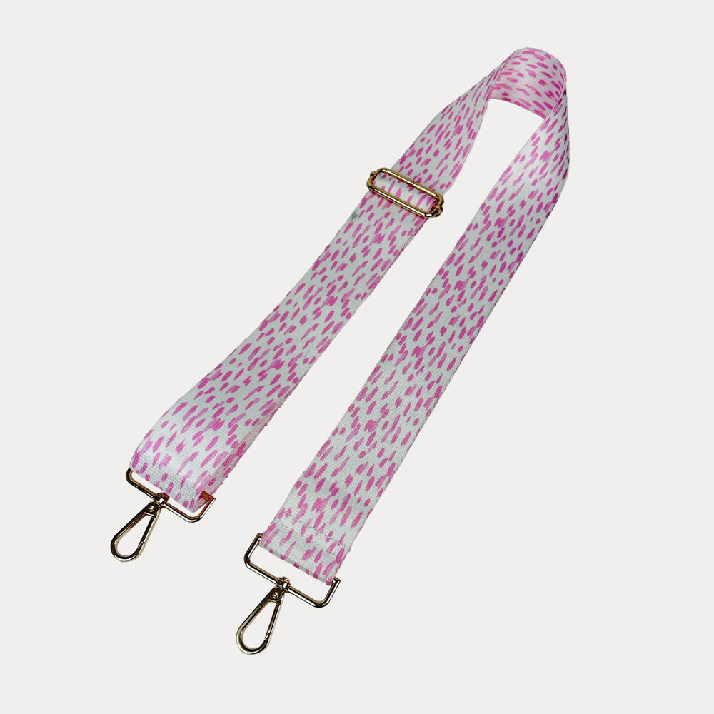 Pink and white dot patterned bag strap with gold hardware on a light gray background