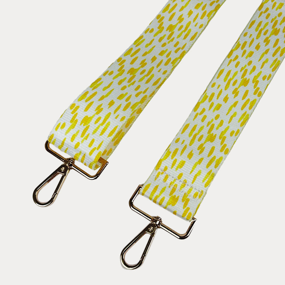 Yellow and white dot patterned bag strap with gold hardware on a light gray background