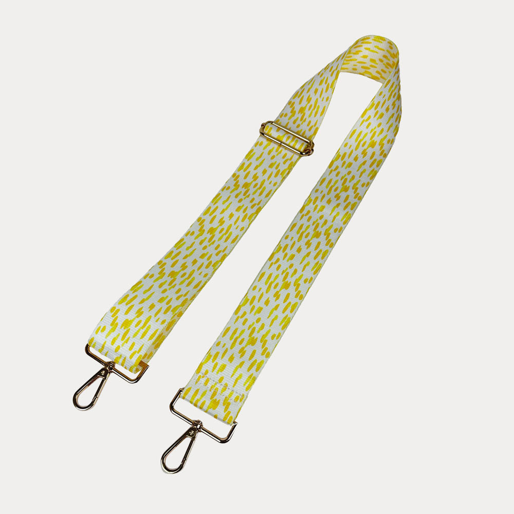 Yellow and white dot patterned bag strap with gold hardware on a light gray background