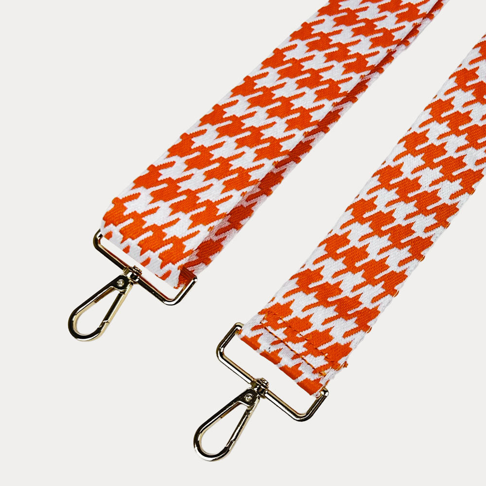 Orange and white houndstooth patterned strap with gold metal clasps on a light gray background