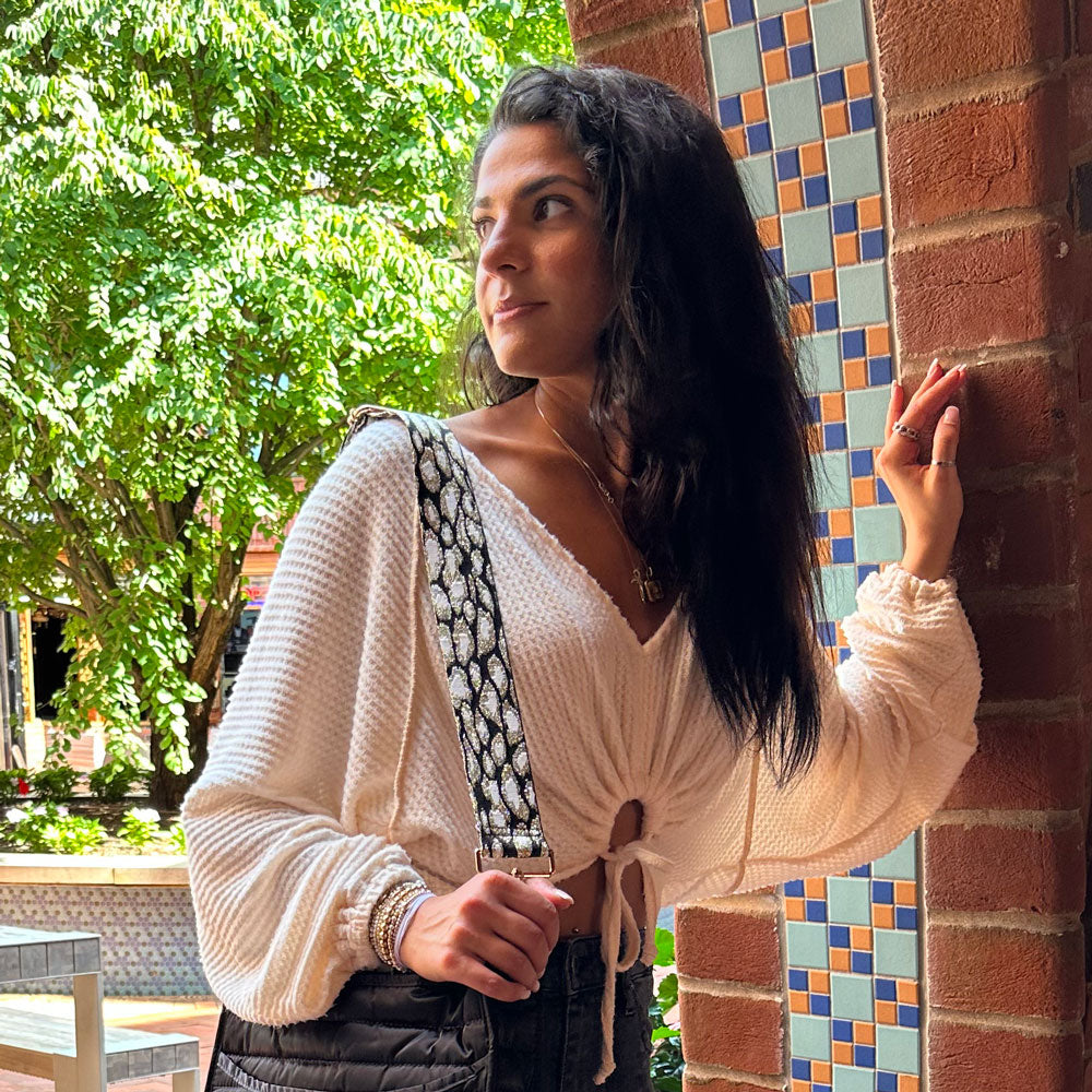 Woman wearing a cream sweater, animal print bag strap and black crossbody bag.