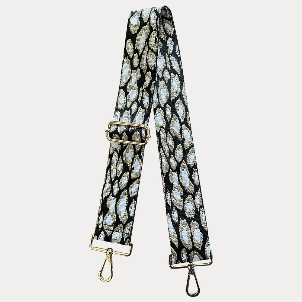 Bag strap with black, gold, and white animal print with gold hardware on a light gray background