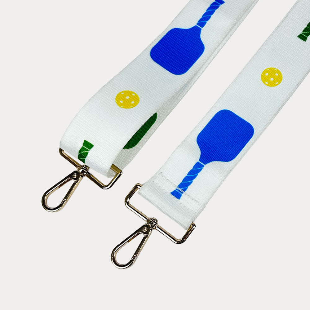 White ground with colorful pickleball paddles and white pickleball graphics with gold hardware bag strap