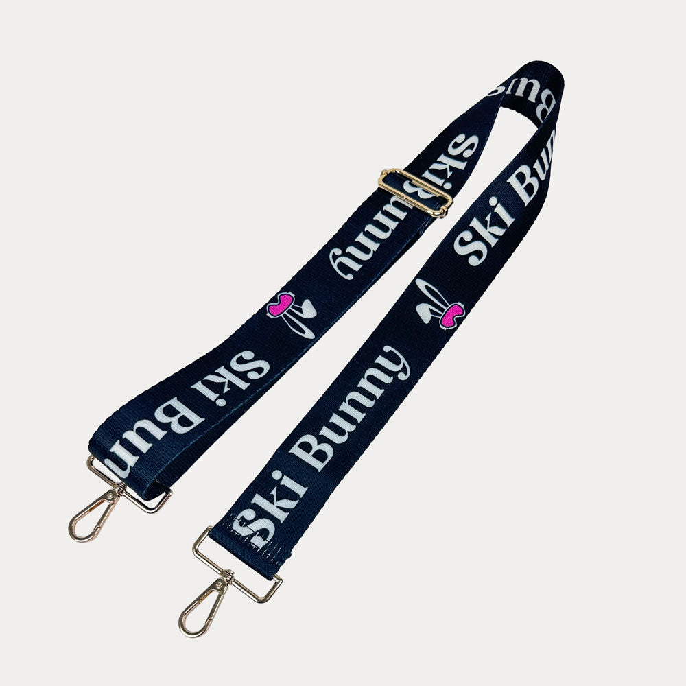 Black ground with Ski Bunny text in White and white bunny with pink accents printed bag strap with gold hardware