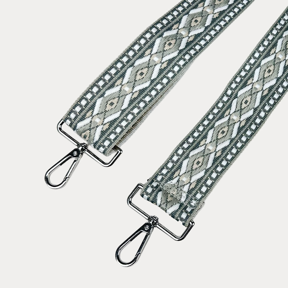 Grey, white, tan diamond patterned bag strap with silver metal clasps on a light gray background