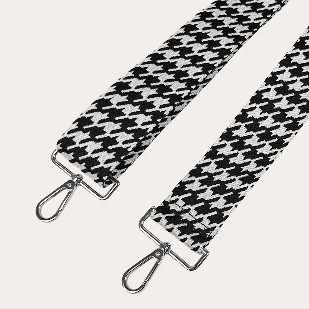 Black and white houndstooth patterned strap with silver metal clasps on a light gray background