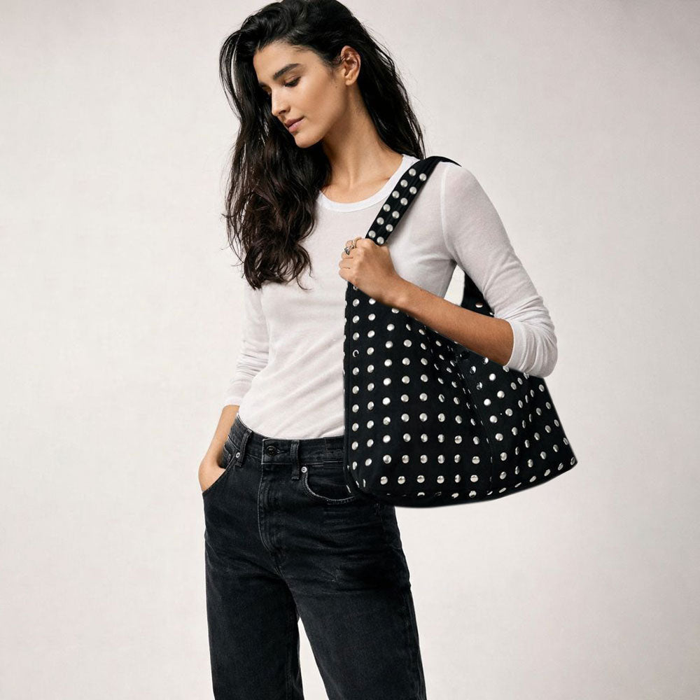 Woman holding a black studded slouchy shoulder bag against a white background