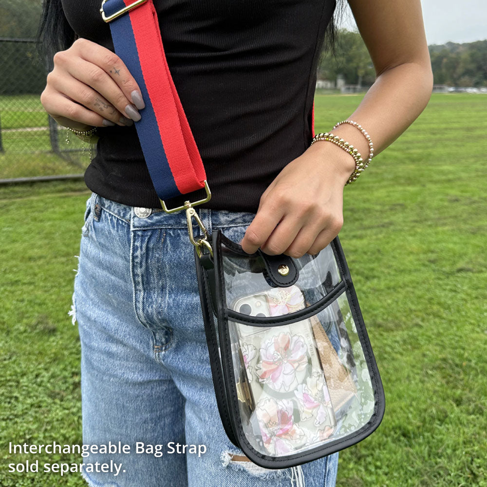 Person holding a clear bag with a red and blue strap, standing in a grassy field.