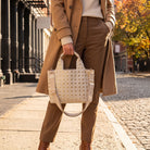 Woman outside on a sunny fall day, standing and holding a cream studded tote.  The image is a close up of the tote.