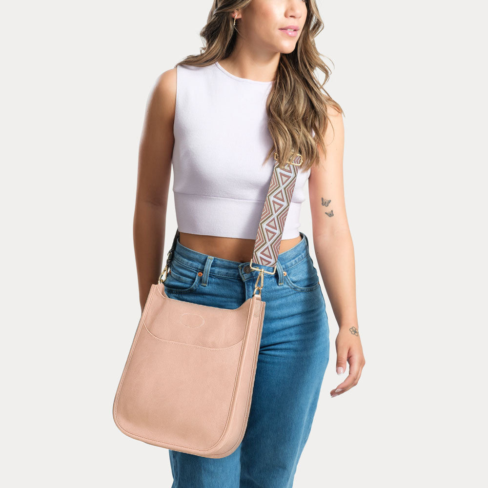 Woman wearing a blush classic messenger with a patterned strap on a white background