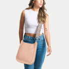Woman wearing a blush classic messenger with a patterned strap on a white background
