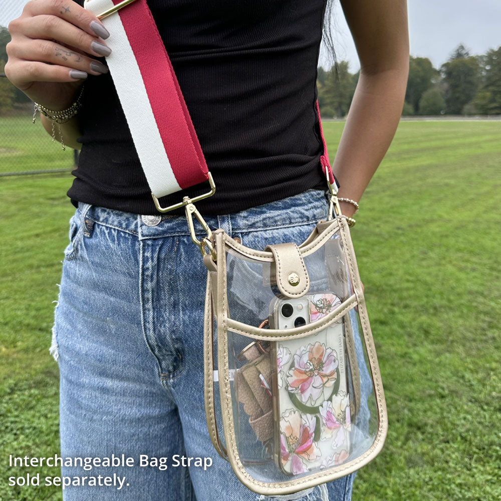 Person holding a transparent crossbody bag with a floral phone case in a grassy field.