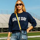 Woman in a stadium outside, wearing a clear messenger bag and striped bag strap. 