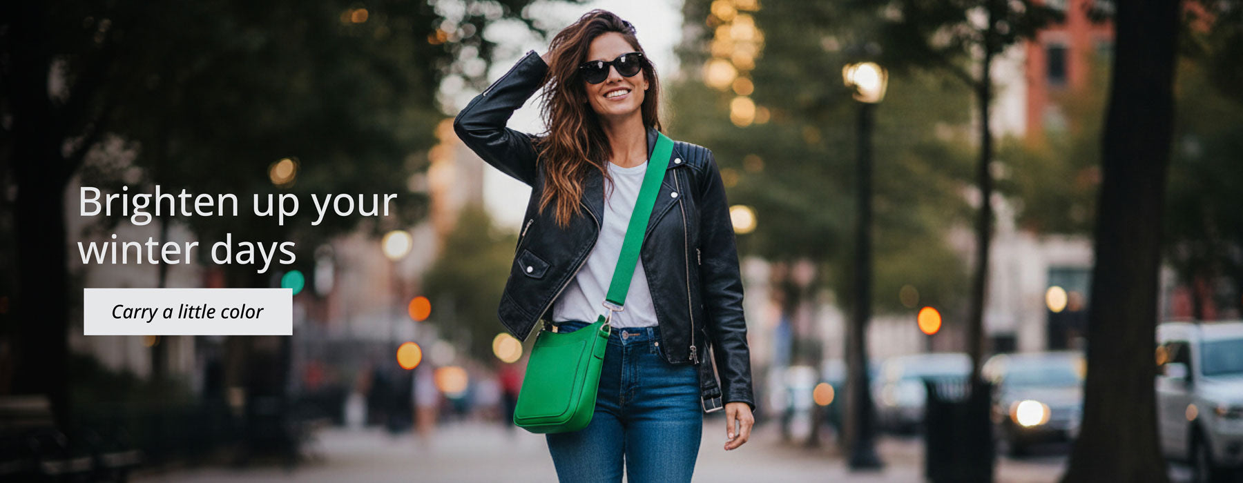Woman walking on a street with a green bag, text 'Brighten up your winter days Carry a little color'.