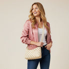 Woman holding a cream handbag with gold studs against a beige background