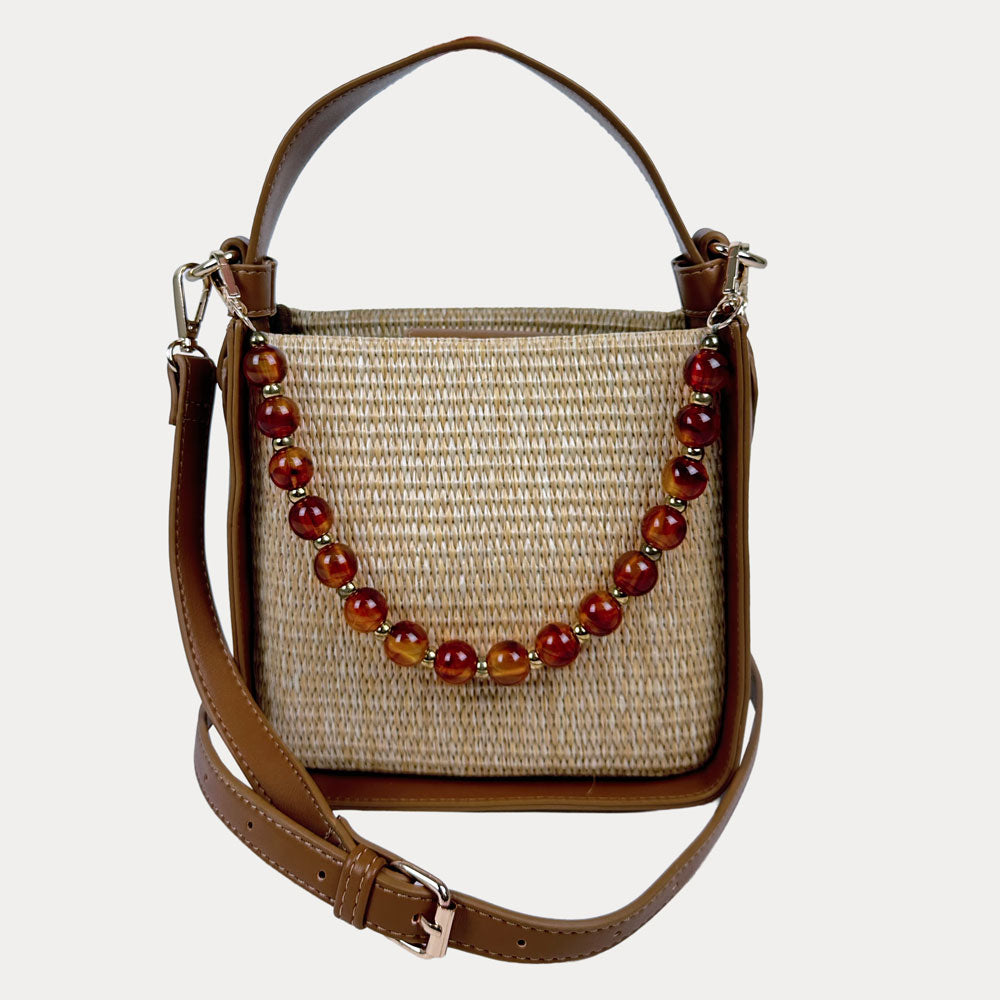 Raffia handbag with Camel Vegan Leather Details and  a beaded strap on a light gray background