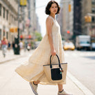 Woman in a cream maxi dress, carrying a Raffia Tote.