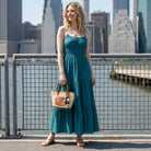 Woman in a teal dress holding a raffia tote with a city skyline in the background