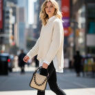 Woman in a cream sweater and black pants walking on a city street. Holding a raffia handbag