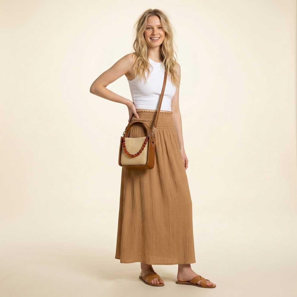 Woman wearing a Raffia handbag, wearing a white top and brown skirt on a beige background