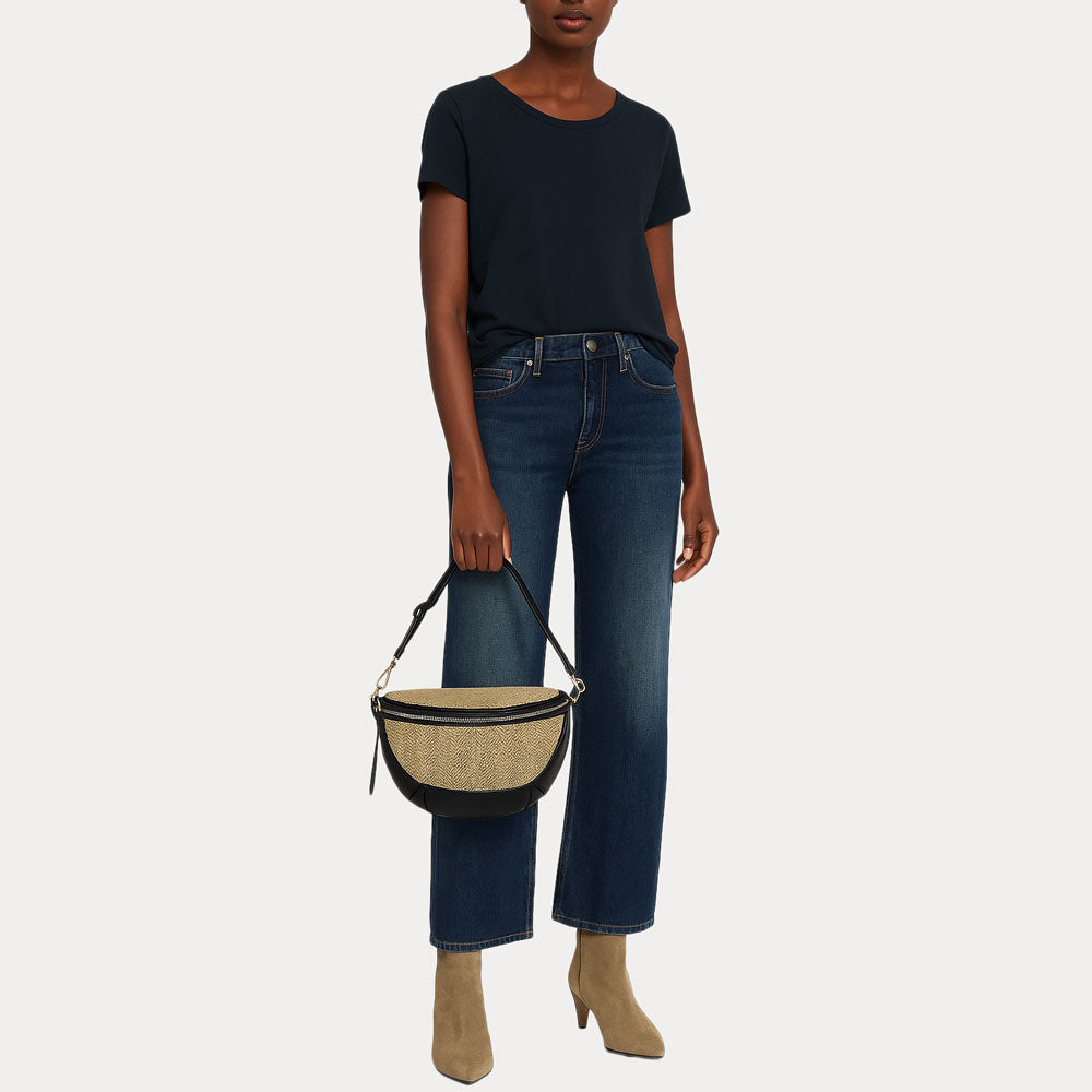 Woman holding a raffia sling bag in her hand down by her side.