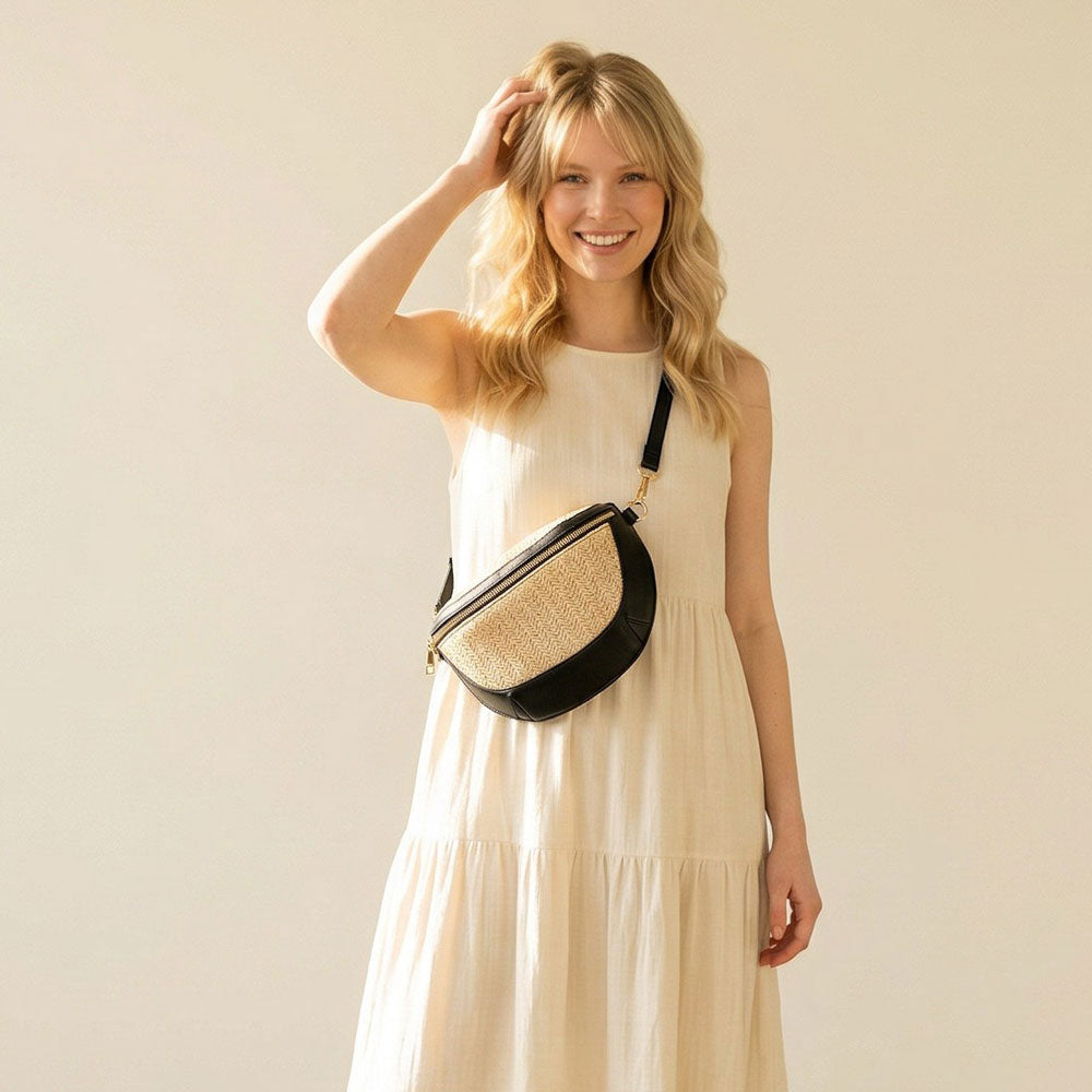 Woman in a beige dress holding a black and raffia sling bag against a plain background