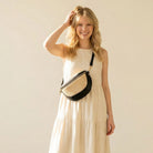 Woman in a beige dress holding a black and raffia sling bag against a plain background