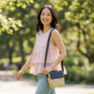 Woman in a pink sleeveless top and jeans wearing a raffia handbag on her shoulder. 