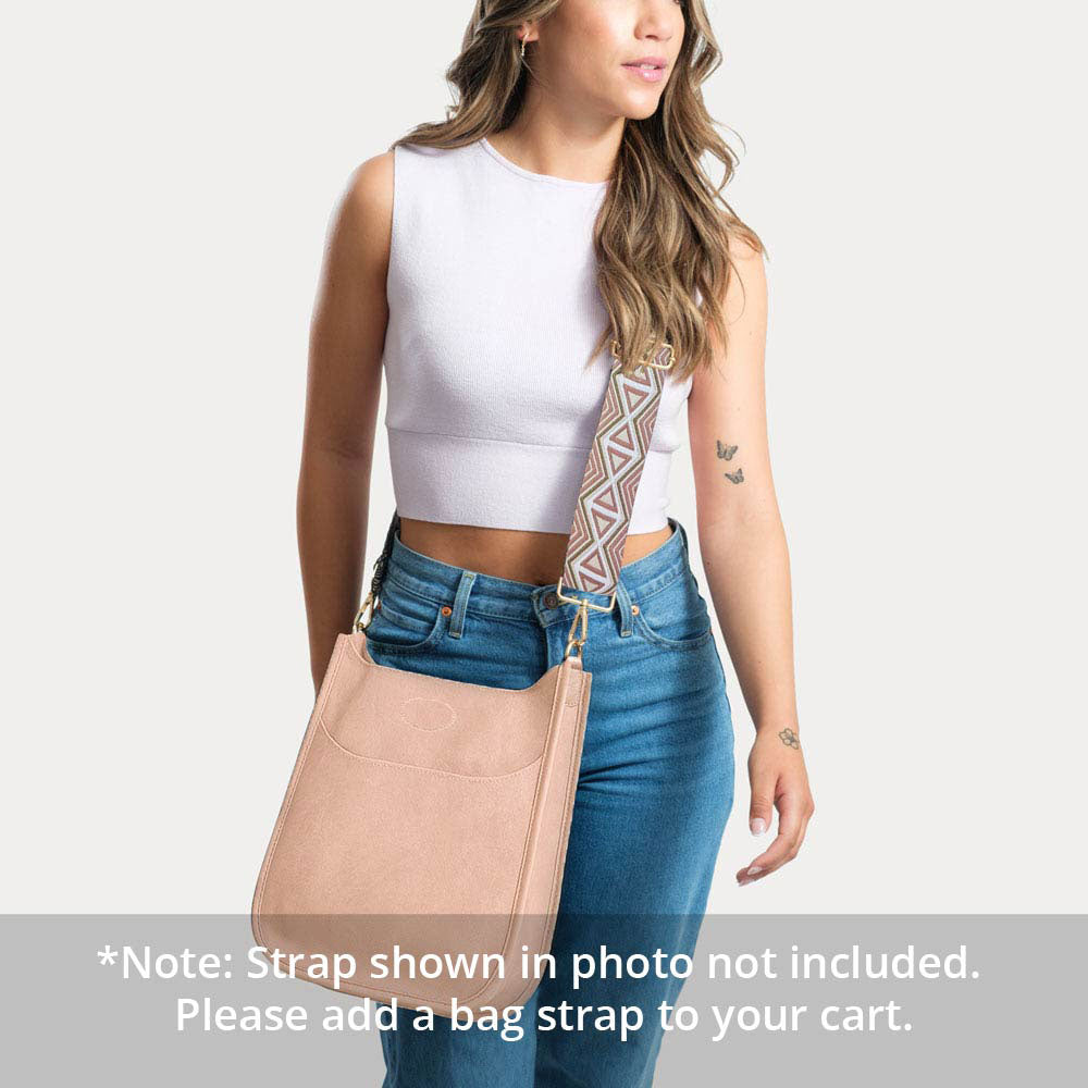 Woman wearing a blush classic messenger with a patterned strap on a white background. Text: Note: Strap Shown in photo not included.  Please add a bag strap to your cart.