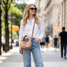 Woman in white shirt and blue jeans holding a deer print handbag on a city street.