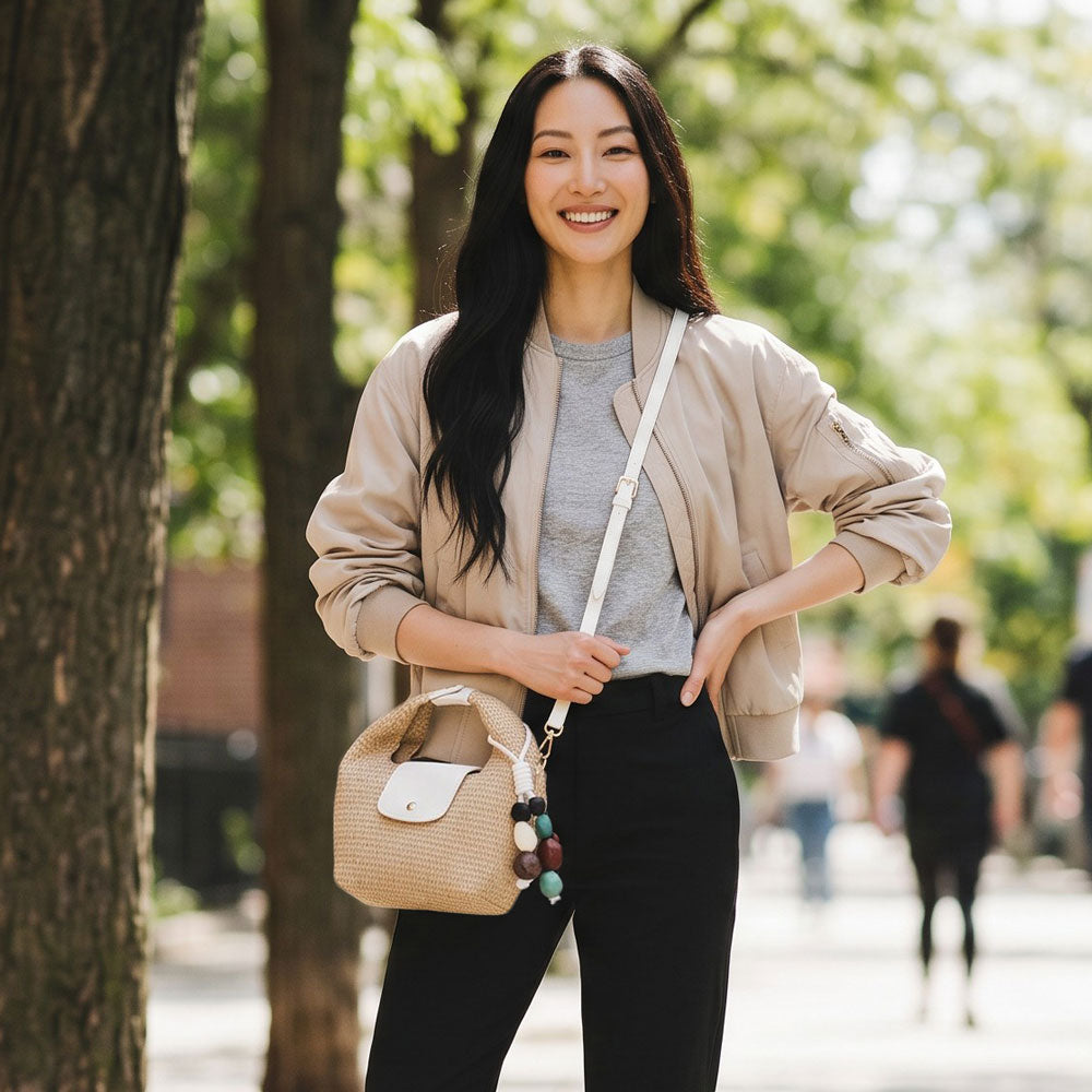 Woman standing outdoors with a raffia handbag, trees in the background