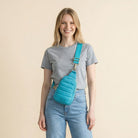 Woman wearing a Turquoise crossbody sling bag against a beige background