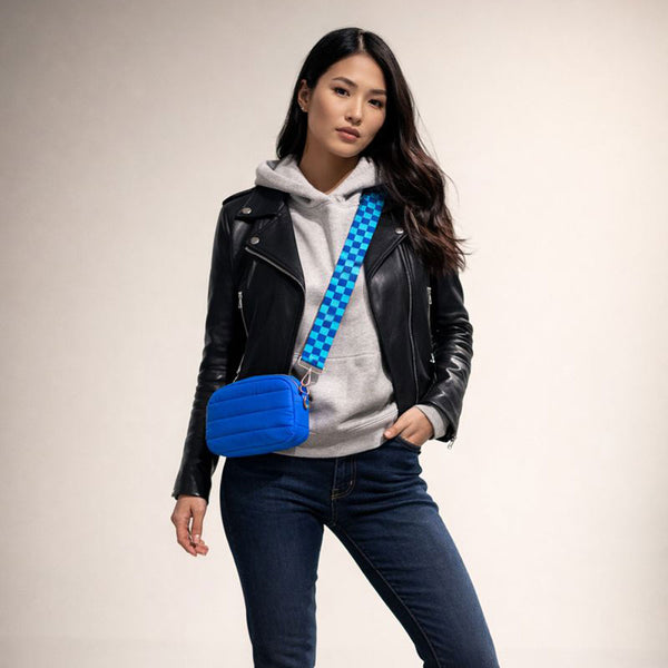 Woman wearing a black leather jacket, gray hoodie, and blue jeans with a blue crossbody bag on a beige background
