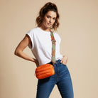 Woman wearing an orange puffer bag with a beige background