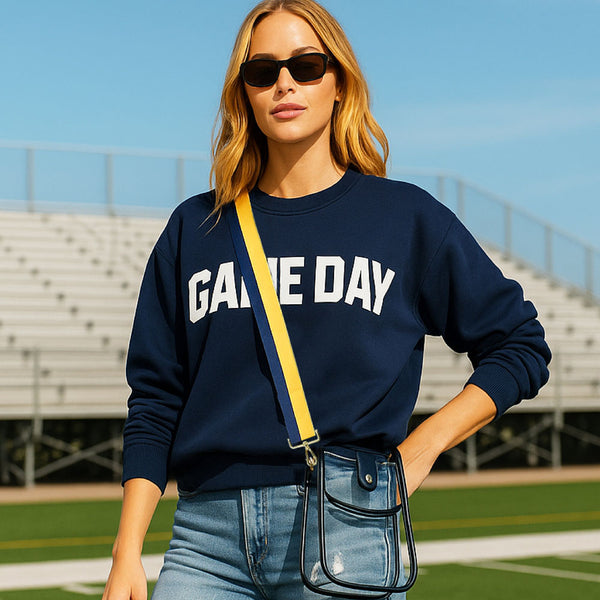 Woman wearing a navy 'GAME DAY' sweatshirt with sunglasses and a clear bag on a sports field.