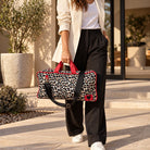 Woman walking outside with a Leopard Print duffle bag with red trim and a black crossbody strap