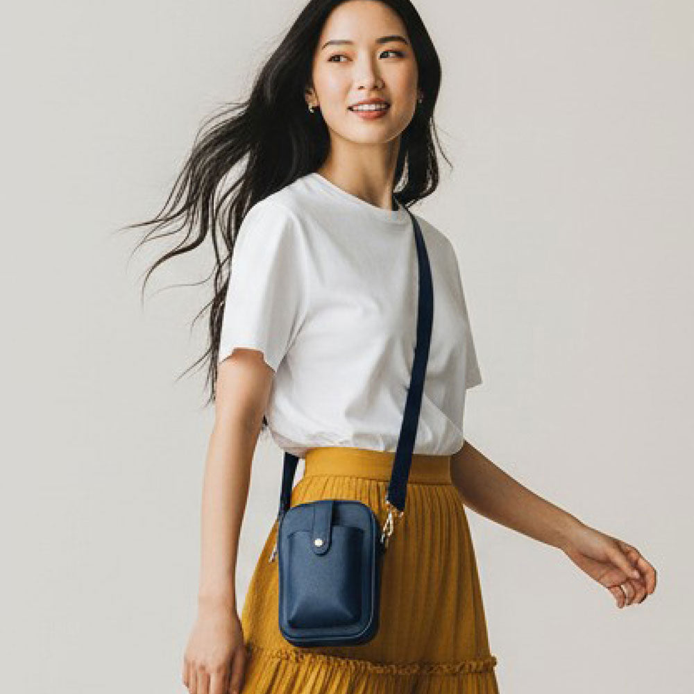 Woman wearing a white shirt and yellow skirt with a navy crossbody bag on a plain background