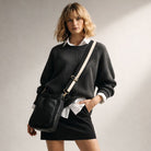 Woman wearing a black sweater and holding a black bag against a neutral background