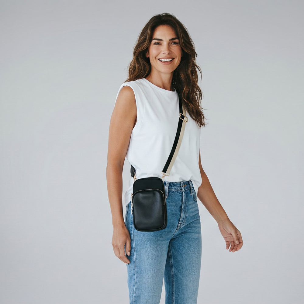 Woman wearing a white sleeveless top and blue jeans with a black crossbody bag on a plain background