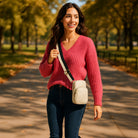 Woman in the park, wearing a cream crossbody bag with a 2 color striped bag strap. 