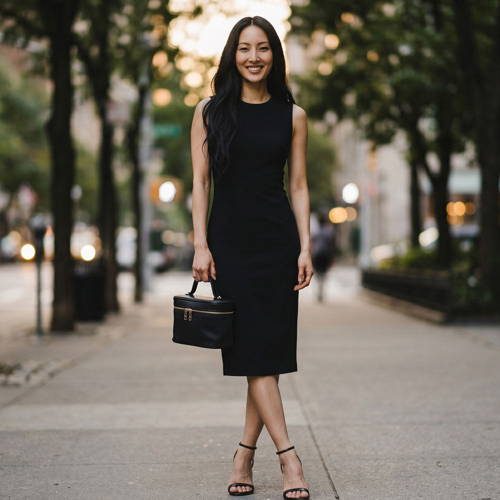 Woman in a black dress holding a black handbag on a city street.