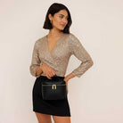 Woman wearing a sparkly top and black skirt holding a black bag against a plain background