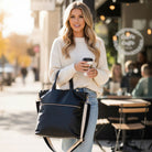 Woman holding a black tote and a coffee cup in an outdoor cafe setting