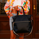 Person holding the black Jill Tote with a colorful jacket and denim shorts.