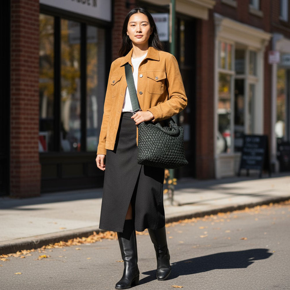 Woman in the city, walking with a army green tote across her body with a crossbody bag strap. 