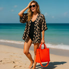 Woman on a beach holding an neon orange tote with ocean in the background