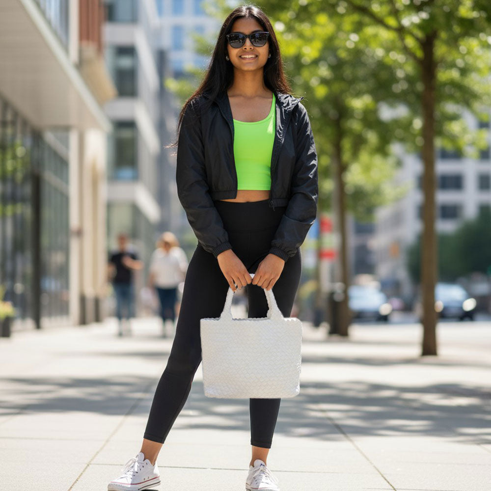Woman in athletic wear holding a white tote on a city street